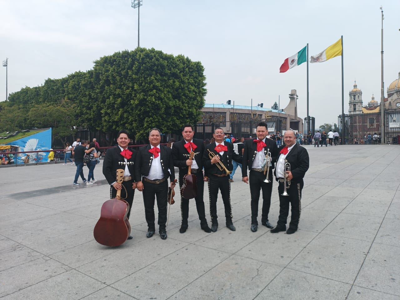 Seis integrantes del Mariachi del Rey con traje de charro negro, moño rojo y sus instrumentos en una plaza de la Ciudad de México